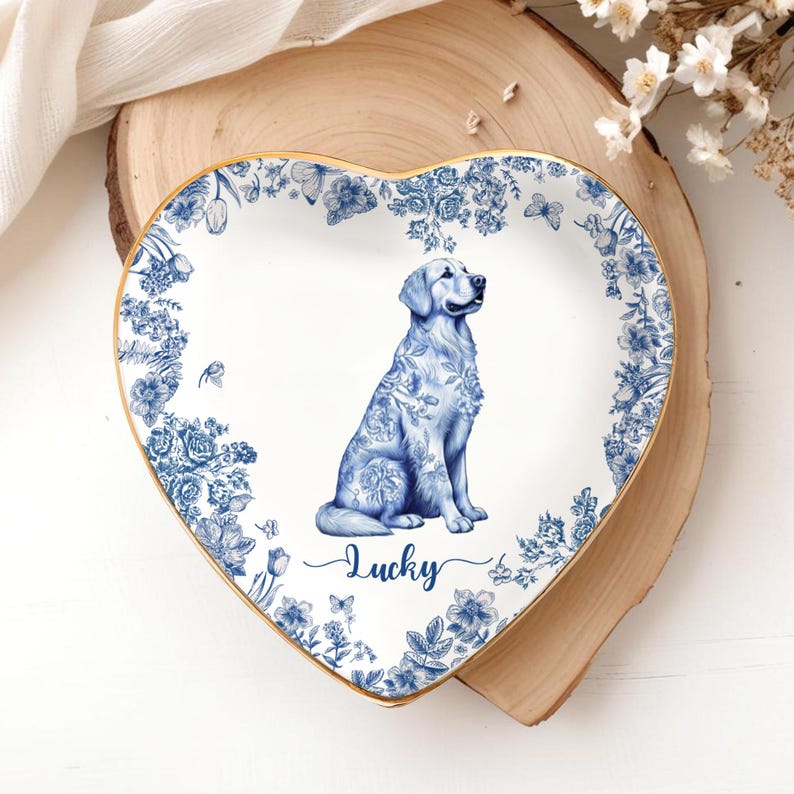 May include: Heart-shaped decorative plate with a blue and white floral design and a golden retriever illustration. The plate has a gold trim and the word "Lucky" in script. The plate is on a wooden surface.