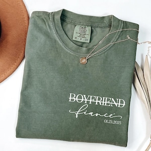 May include: A green t-shirt with the text "BOYFRIEND fiance 01.23.2025" printed on the front.