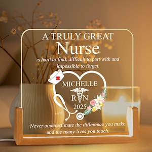 May include: A white acrylic plaque with a wooden frame, featuring a quote about nurses. The plaque has a heart with a stethoscope, a caduceus, and the text "Michelle RN 2025".