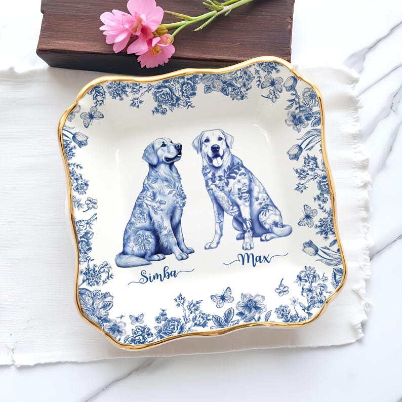 May include: Square ceramic serving dish with a blue and white floral design and gold trim. Features illustrations of two dogs, with the names "Simba" and "Max" below. The dish is decorated with butterflies and flowers.