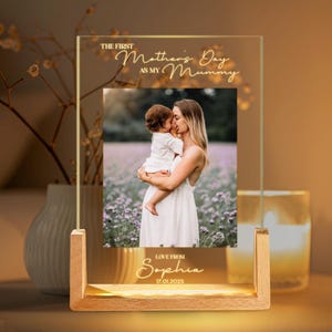May include: A glass photo frame with a wooden base, featuring a photo of a mother and child. The frame has a gold inscription that reads "The First Mother's Day as My Mummy" and "Love From Sophia 17.01.2025".