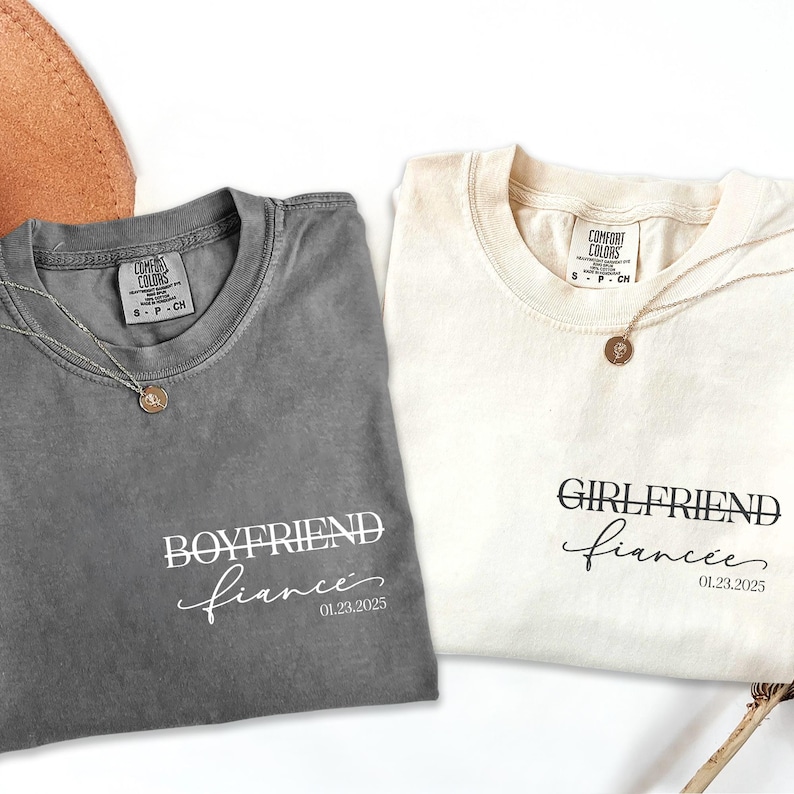 May include: Two t-shirts, one gray and one cream, with the text "Boyfriend fiance 01.23.2025" and "Girlfriend fiancee 01.23.2025" printed on them.