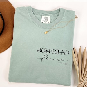 May include: A light green t-shirt with the text "Boyfriend fiance" and the date "01.23.2025" printed on it.