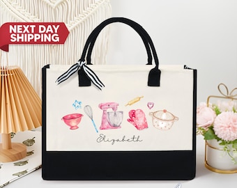 May include: A white canvas tote bag with black handles and a black bottom. The bag has a watercolor design of kitchen tools, including a mixer, rolling pin, whisk, and oven mitts. The name "Elizabeth" is printed in black below the design.