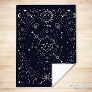 May include: A black fleece blanket with a white design of a zodiac constellation for Aries. The design includes a ram, stars, and the words "Aries" and "Elizabe".