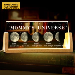 May include: A wooden light-up sign with the text "Mommy's Universe" and five moons representing family members. Each moon has a name and date, such as "Luke June 26th 1980".