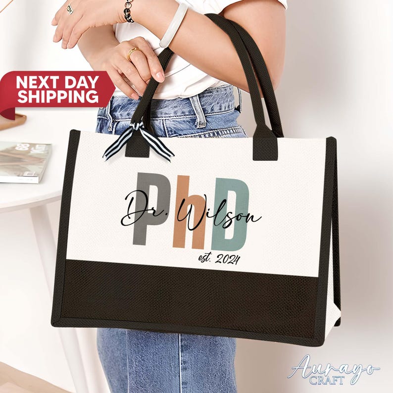 Pode incluir: Sacola de lona branca com al&ccedil;as pretas e um painel inferior preto. A sacola tem um design personalizado com o texto "Dr. Wilson PhD est. 2024" em letras coloridas.