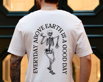 May include: White t-shirt with a black skeleton graphic and the text "EVERYDAY ABOVE EARTH IS A GOOD DAY".