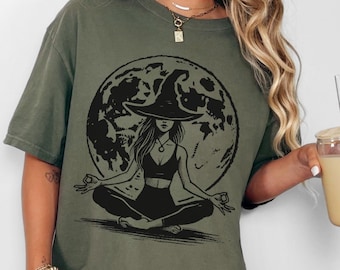 May include: Sage green oversized t-shirt featuring a black graphic of a witch meditating in front of a full moon.