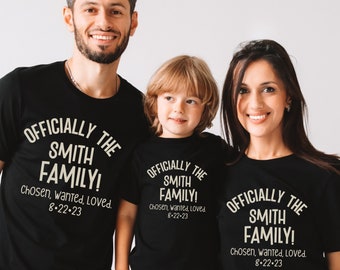 Puede incluir: Tres camisetas negras con el texto "Officially the Smith Family! Chosen, wanted, loved. 8-22-23" impreso en blanco. Las camisetas las lleva una familia de tres.