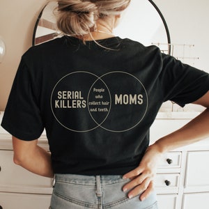 Puede incluir: Una camiseta negra con un gr&aacute;fico de diagrama de Venn que dice "Asesinos en serie" y "Mam&aacute;s" con la secci&oacute;n superpuesta que dice "Personas que recolectan cabello y dientes."