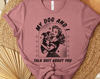 May include: Heather mauve t-shirt with a black and white graphic of a woman holding a dog. The graphic says "My Dog And I Talk Shit About You".