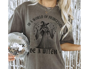 May include: A gray t-shirt with a black graphic of a witch with the text "In a world of princesses be a witch".