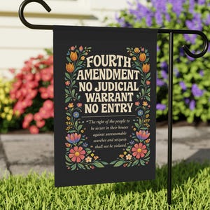 Op de afbeelding: Een zwarte tuin vlag met de tekst "FOURTH AMENDMENT NO JUDICIAL WARRANT NO ENTRY" in het wit, omringd door bloemmotieven. De vlag bevat ook een citaat over onredelijke huiszoekingen en inbeslagnames.
