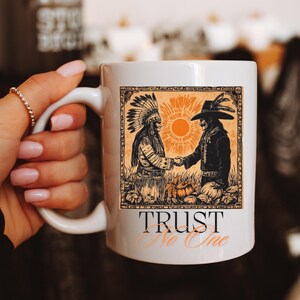 Könnte beinhalten: Weiße Keramik-Tasse mit einer Illustration im Vintage-Stil von zwei Figuren, die sich die Hände schütteln, mit einer Sonne im Hintergrund. Die Tasse trägt den Text "TRUST No One". Das Design ist in Orange-, Schwarz- und Beigetönen gehalten.