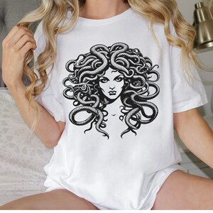 May include: White t-shirt with a black and white graphic print of Medusa, a mythical Greek figure with snakes for hair.