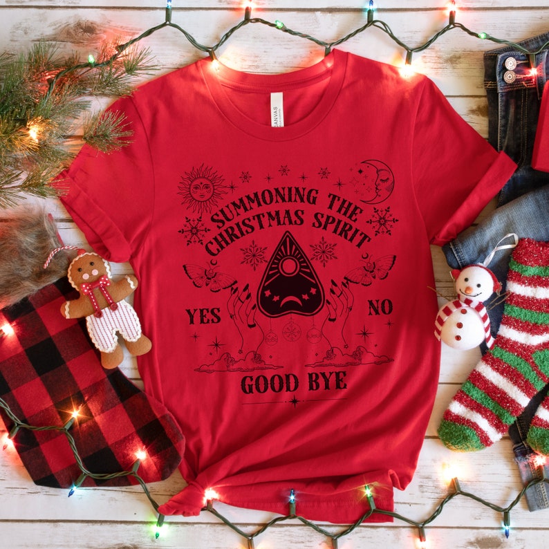 May include: Red t-shirt with a black graphic of a Ouija board with the text "Summoning the Christmas Spirit" and "Good Bye" on a white background.