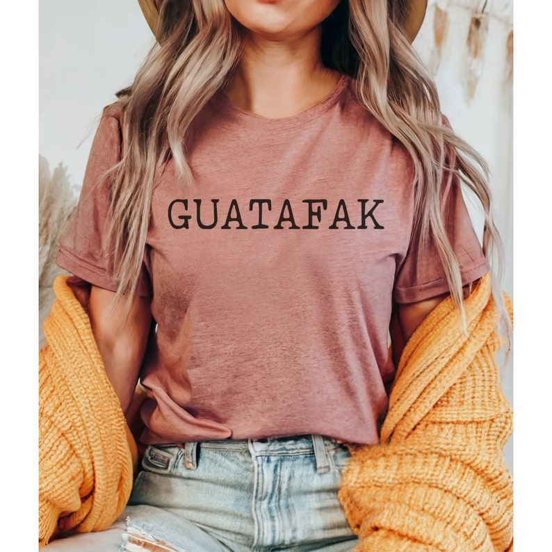 May include: A mauve colored t-shirt with the text "GUATAFAK" printed in black.