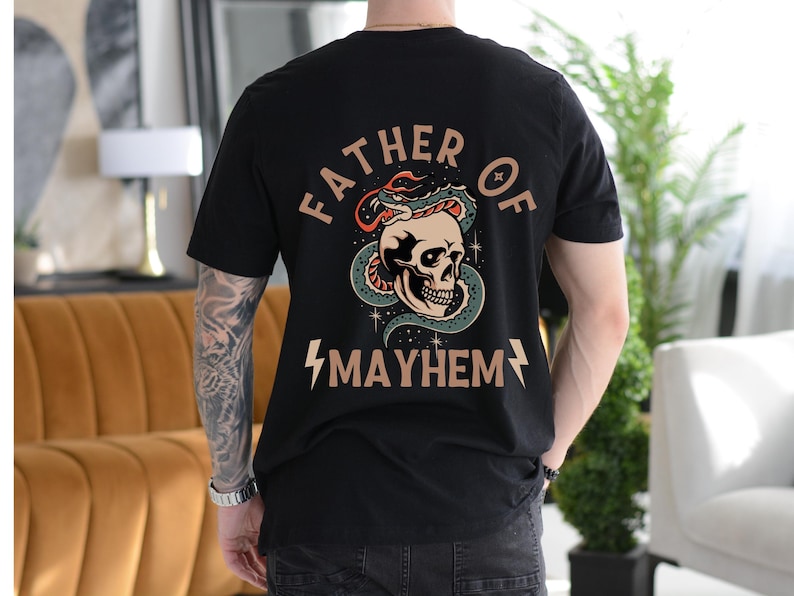 以下が含まれることがあります： 骸骨に蛇が巻き付いているグラフィックプリントが施された黒いTシャツ。骸骨の下に「Father of Mayhem」という文字がプリントされています。