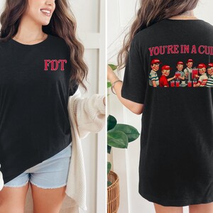 K&ouml;nnte beinhalten: Schwarzes T-Shirt mit dem Text "FDT" auf der Vorderseite und "YOU'RE IN A CULT" mit einem Vintage-Bild von Kindern, die ein Getr&auml;nk trinken, auf der R&uuml;ckseite.