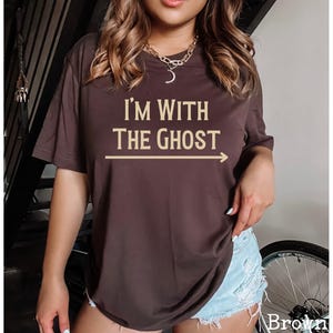 May include: A brown t-shirt with the text "I'm with the ghost" in a light brown color. An arrow points to the right of the text.