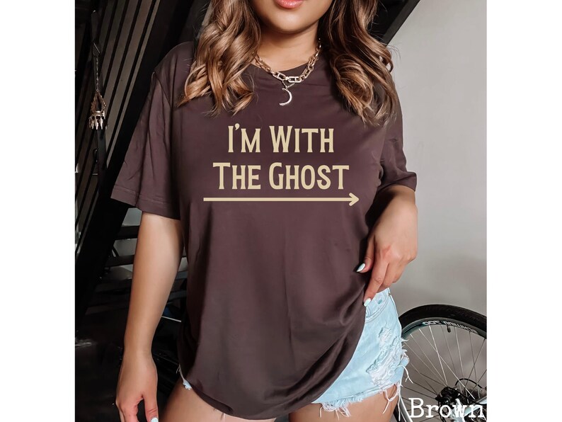 May include: A brown t-shirt with the text "I'm with the ghost" in a light brown color. An arrow points to the right of the text.