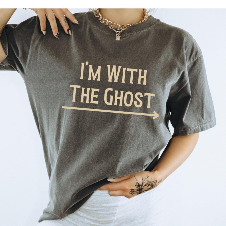 May include: A dark gray t-shirt with the text "I'm with the ghost" printed in a light yellow color. An arrow points to the right of the text.