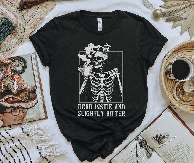 May include: Black t-shirt with a skeleton holding a cup of coffee. The text "Dead inside and slightly bitter" is printed below the skeleton.