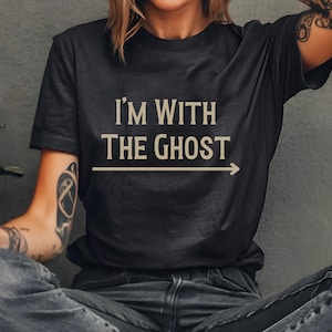 May include: A black t-shirt with the text "I'm with the Ghost" printed in beige with an arrow pointing to the right.