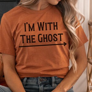 May include: A rust-colored t-shirt with the text "I'm with the ghost" and an arrow pointing to the right.