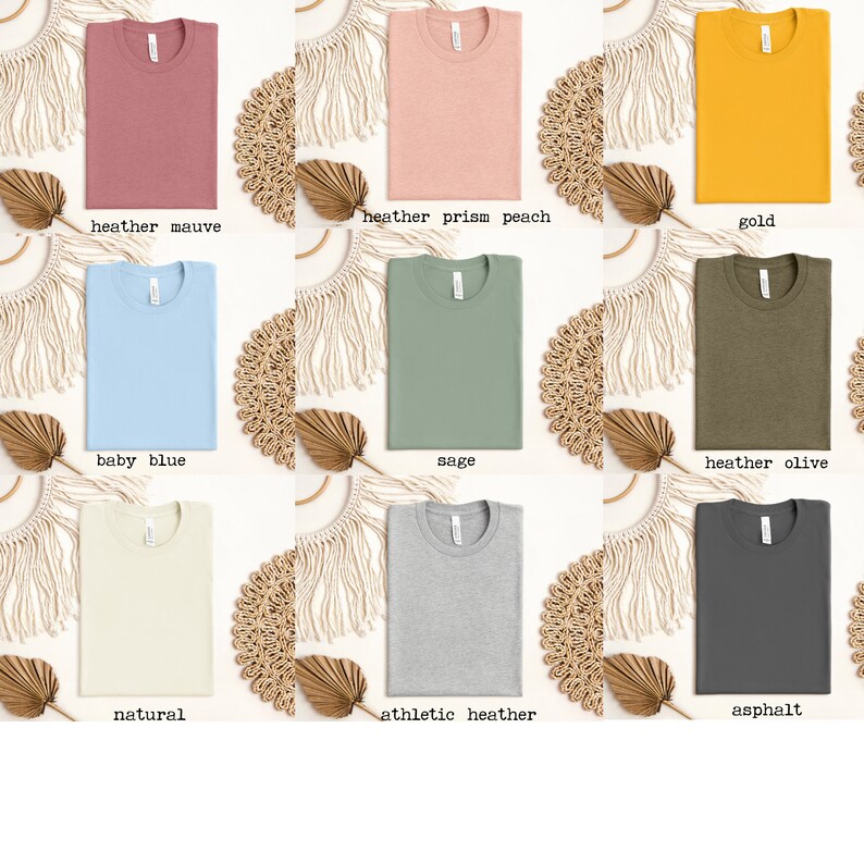 Op de afbeelding: Negen gevouwen T-shirts in verschillende kleuren, waaronder heidepaars, heideperzik, goud, babyblauw, salie, heidegroen, naturel, sportgrijs en asfalt.