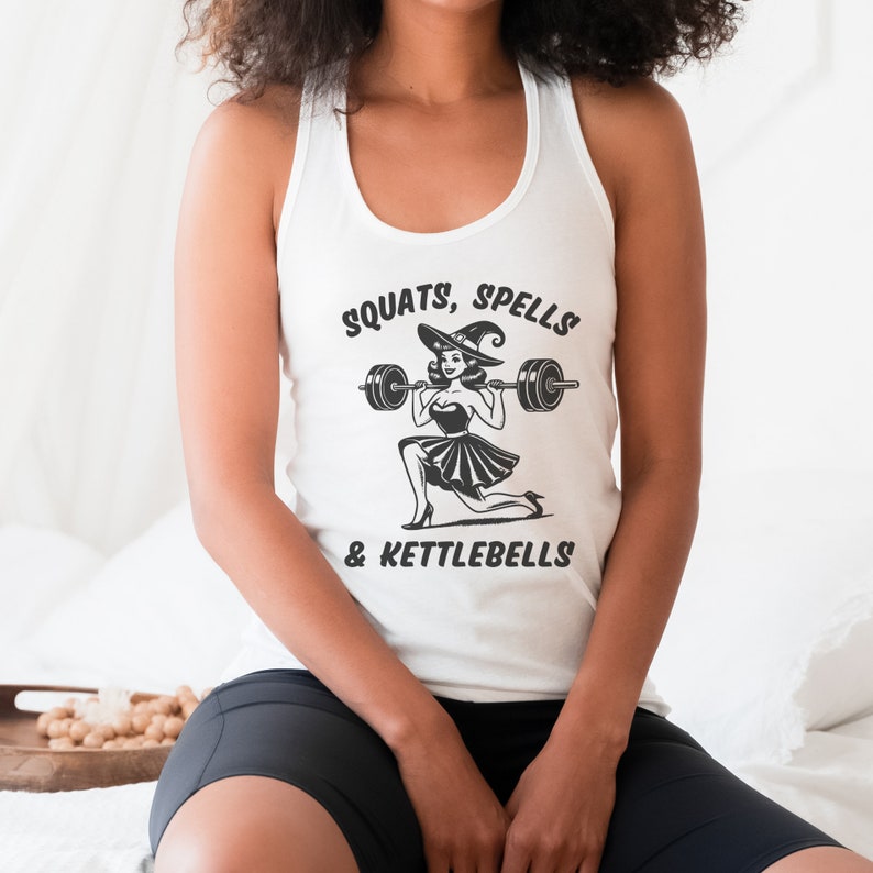 May include: White tank top with a black and white illustration of a witch lifting a barbell. The text "SQUATS, SPELLS & KETTLEBELLS" is printed on the shirt.