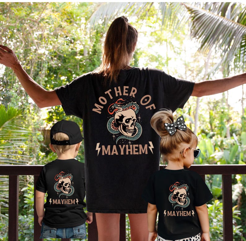 以下が含まれることがあります： 骸骨とヘビのグラフィックと「Mother of Mayhem」のテキストが書かれた、家族向けのブラックTシャツのマッチングセットです。