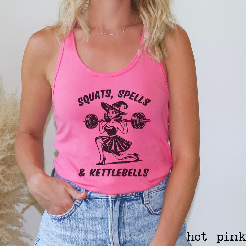 May include: A pink tank top with a black graphic of a witch lifting a barbell. The text on the tank top reads "Squats, Spells & Kettlebells".