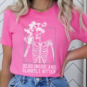 May include: A pink t-shirt with a white skeleton holding a coffee cup and the text "Dead inside and slightly bitter".