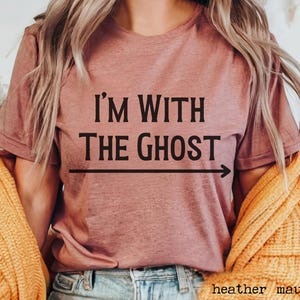 May include: A heather mauve t-shirt with the text "I'm with the ghost" and an arrow pointing to the right.