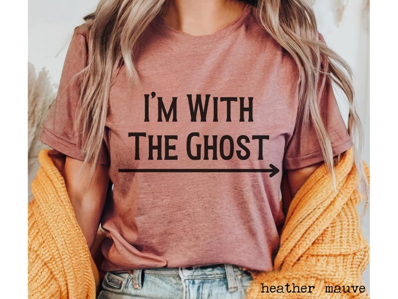 May include: A heather mauve t-shirt with the text "I'm with the ghost" and an arrow pointing to the right.