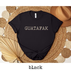 May include: Black t-shirt with the text "GUATAFAK" printed in a light beige color.