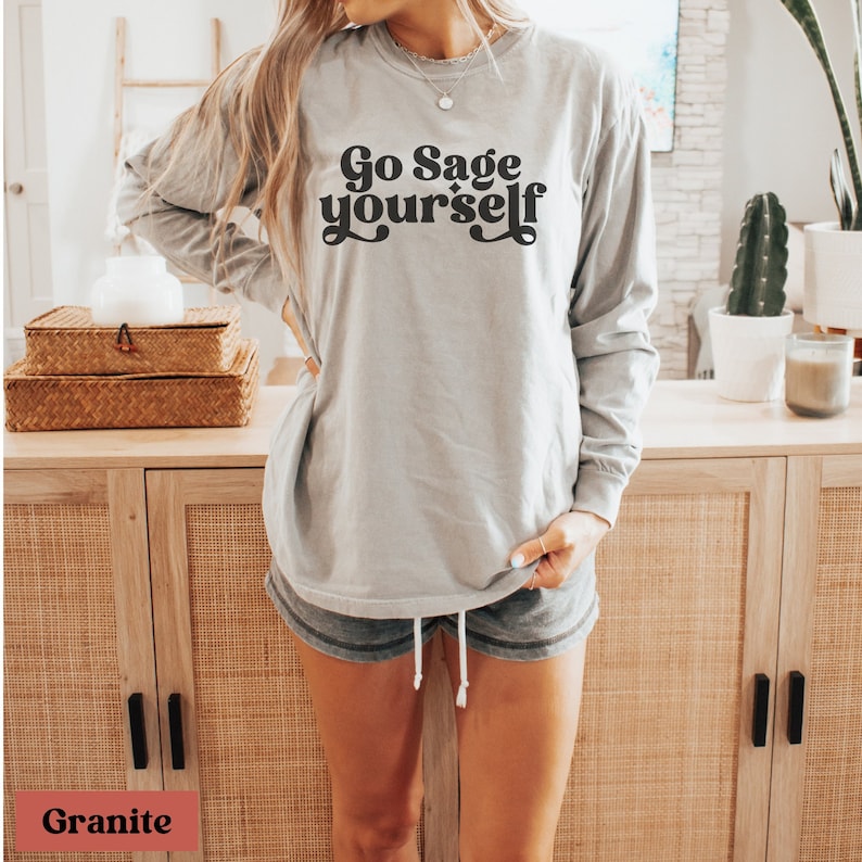 May include: A gray long-sleeve t-shirt with the text "Go Sage Yourself" in black retro-style lettering.