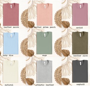 May include: A collection of ten blank t-shirts in various colors, including heather mauve, prism peach, orchid, baby blue, sage, heather olive, natural, athletic heather, and asphalt.