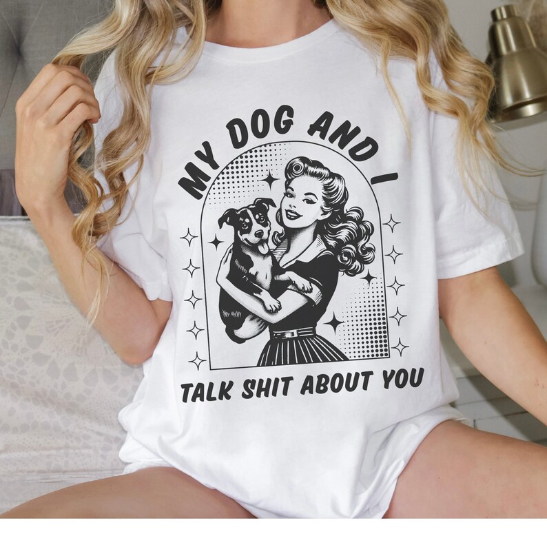 Op de afbeelding: Wit T-shirt met een zwart-witte afbeelding van een vrouw die een hond vasthoudt. De afbeelding zegt "My Dog And I Talk Shit About You".