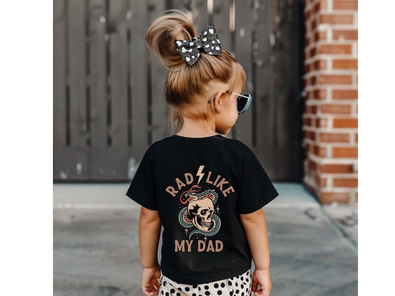 May include: A black t-shirt with a graphic of a skull with a snake wrapped around it. The text "Rad Like My Dad" is printed on the shirt.