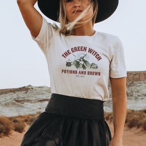 May include: White t-shirt with a green witch graphic and the text "The Green Witch Potions and Brews Est. 1626".