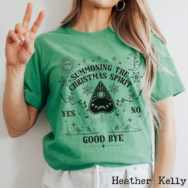 May include: Green t-shirt with a black graphic design of a Ouija board with the text "Summoning the Christmas Spirit" and "Good Bye" on a green background.