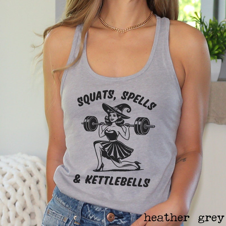 May include: A heather grey tank top with a black and white graphic of a witch lifting weights. The text on the tank top reads "SQUATS, SPELLS & KETTLEBELLS".