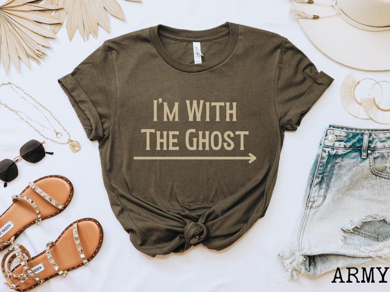 May include: A dark green t-shirt with the text "I'm with the Ghost" in beige lettering and an arrow pointing to the right. The shirt is made of a soft, comfortable material.
