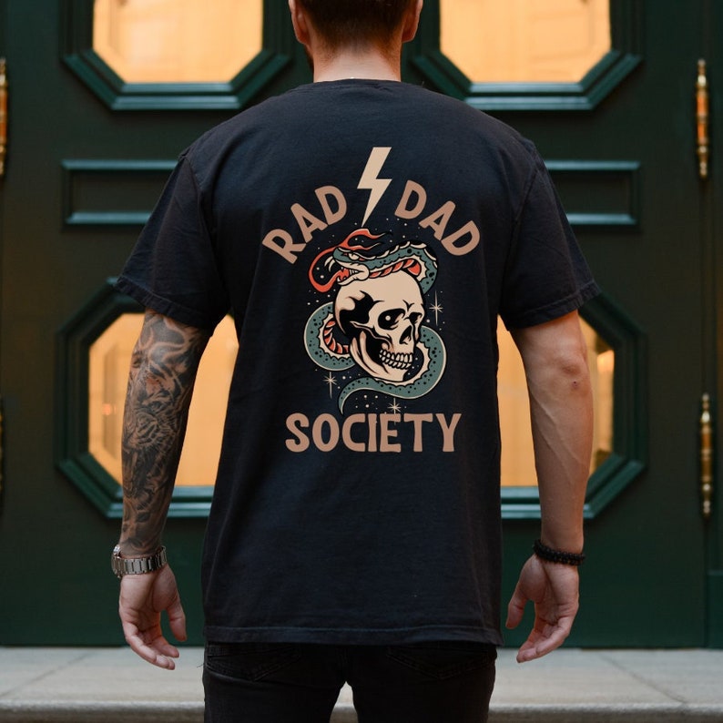 May include: Black t-shirt with a graphic print of a skull with a snake wrapped around it. The text "RAD DAD SOCIETY" is printed on the shirt.