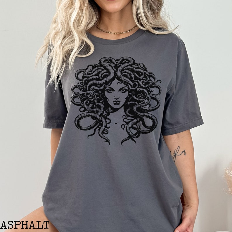 May include: A dark gray t-shirt with a black and white graphic print of Medusa, a mythical Greek figure with snakes for hair.