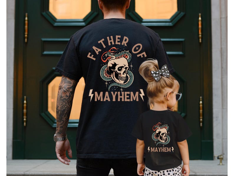 以下が含まれることがあります： 「Father of Mayhem」という文字と、蛇が巻き付いた頭蓋骨が描かれた黒いTシャツ。同じデザインの黒いTシャツを子供が着ています。