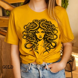 May include: A yellow t-shirt with a black graphic of Medusa, a mythical Greek figure with snakes for hair.